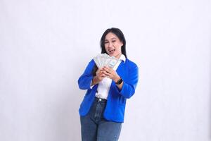 beautiful adult office woman wearing blue formal suit standing cheerfully to camera both hands holding dollar bills in front of white background isolation. for transaction, finance, business content photo