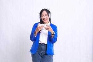 beautiful adult office girl wearing blue formal suit standing happily operating smartphone mobile phone and headphone isolation white background. technology, lifestyle, music, entertainment content photo