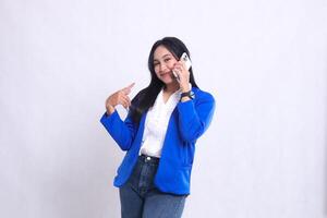 beautiful mature office woman wearing blue formal suit standing smiling to camera while using smartphone phone while pointing at it isolated white background. for technology, lifestyle, communication photo