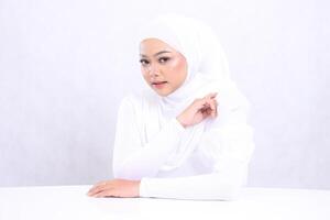 The charm of a veiled female indonesia focuses on the front with perfect and healthy white skin, hands on the table and left arm isolated on a white background. Closeup of a face makeup for skincare photo