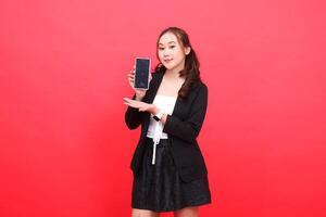 expression of young asian career woman smiling at the camera wearing black formal suit holding smartphone while introducing, for technology, business, advertising, financial content photo