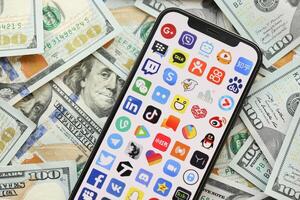 KYIV, UKRAINE - APRIL 1, 2024 Many apps icon on smartphone screen on many usd money bills photo