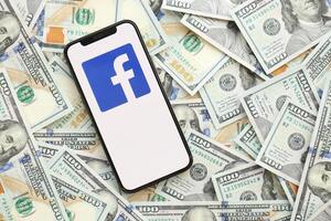KYIV, UKRAINE - APRIL 1, 2024 Facebook icon on smartphone screen on many usd money bills photo