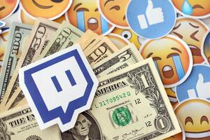 KYIV, UKRAINE - APRIL 20, 2024 Twitch logo and many usd money bills. Symbol of famous social network platform and dollar currency banknotes on lot of emoji reactions photo