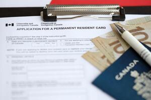 Application for permanent resident card on table with pen and canadian passport with money photo