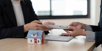 Real Estate Agent Handing Over Money for Property Sale with House Model on Desk in Office Setting photo