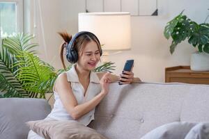 Young Woman Relaxing on Sofa with Headphones and Smartphone in Modern Living Room with Green Plants photo
