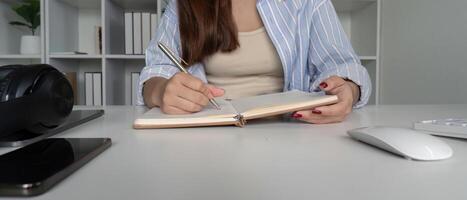 Young Student Studying Online at Home, Taking Notes in Notebook, Using Laptop and Headphones for Learning photo