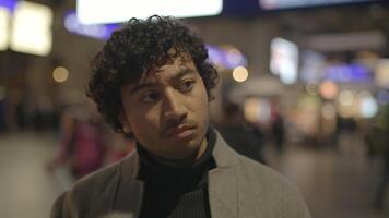 A contemplative man appears in a crowded urban setting with vibrant neon signs in the background video