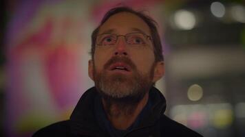 A man gazes at the night sky with a thoughtful look, city lights in the background video