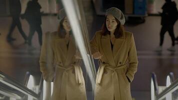 A stylish woman in a beige coat and hat is seen on an escalator in a modern urban environment video
