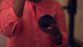 A woman is applying makeup with a handheld compact mirror as part of her beauty routine video