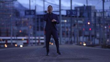 A businessperson is having a phone conversation at a train station during the evening video