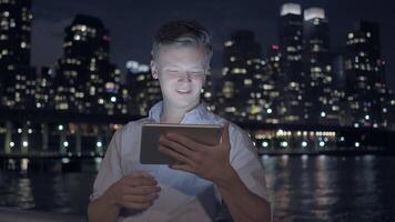 In the evening, a man is engrossed using a tablet under the dazzling glow of city lights video
