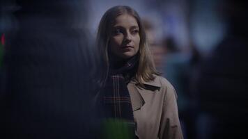 A young woman, dressed in a coat and scarf, standing in an urban evening setting video