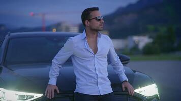 A Stylish Man Posing by a Luxury Car at Dusk, exuding confidence and charm in an urban setting video