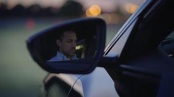 A Man is Using His Phone, Reflected in the Side Mirror of a Car During Dusk Hours video