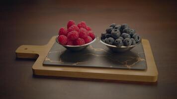 Fresh Raspberries and Blueberries are carefully arranged in Metal Bowls on a Wooden Board video