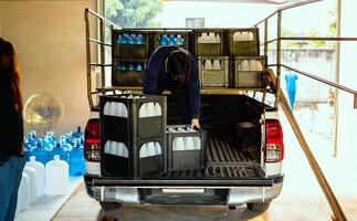 Workers lift drinking water bottles in crates into the back of a transport truck purified drinking water inside the production line to prepare for sale. Water drink factory, small business photo