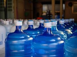 Many blue gallons and white gallon of drinking water are lined up in a drinking water production plant. photo