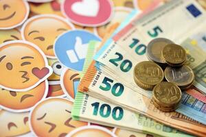 KYIV, UKRAINE - APRIL 20, 2024 European euro money and large set of stickers with Emoji yellow faces. The concept of smm, smo paid service for boost in social media photo