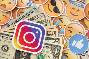 KYIV, UKRAINE - APRIL 20, 2024 Instagram logo and many usd money bills. Symbol of famous social network platform and dollar currency banknotes on lot of emoji reactions photo