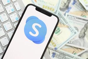 KYIV, UKRAINE - APRIL 1, 2024 Skype icon on smartphone screen on many usd money bills photo