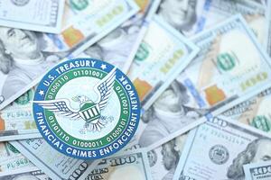 KYIV, UKRAINE - JUNE 26, 2024 U.S. Treasury Financial Crimes Enforcement Network coat of arms on big amount of US dollar banknotes photo