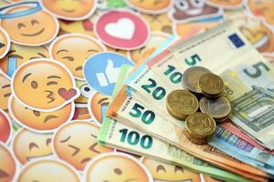 KYIV, UKRAINE - APRIL 20, 2024 European euro money and large set of stickers with Emoji yellow faces. The concept of smm, smo paid service for boost in social media photo