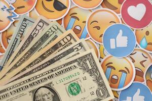 KYIV, UKRAINE - APRIL 20, 2024 USD dollars money and large set of stickers with Emoji yellow faces. The concept of smm, smo paid service for boost in social media photo