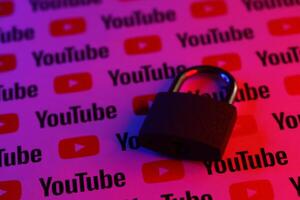 KYIV, UKRAINE - NOVEMBER 27, 2023 Locked small lock on many Youtube logotypes in red and blue light photo