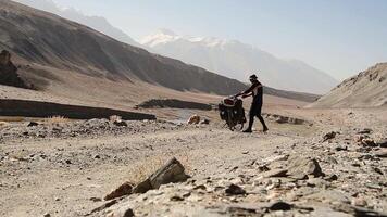 Back view adventurous caucasian male traveller cycle bicycle touring solo on gravel terrain famous Pamir highway Bartang valley in remote high Pamir mountains. Pamir highway adventure travel route video