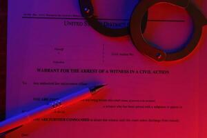 District court warrant for the arrest of a witness in a civil action papers with handcuffs and blue pen on United States flag. Permission to witness photo