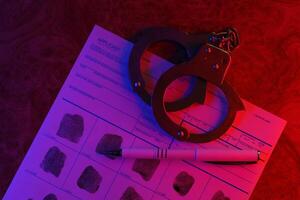 Applicant or fingerprints card with police handcuffs on table in dark room photo