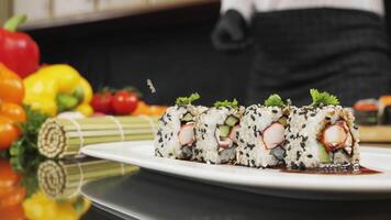 Chef's hands sprinkle sesame seeds on the inside out sushi. Japanese chef in black gloves at work preparing sushi roll with salmon and avocado. video