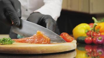 Professional chef uses a kitchen knife to cut the salmon. Fresh raw salmon fillet on a wooden chopping board. Low angle shot in 4K video