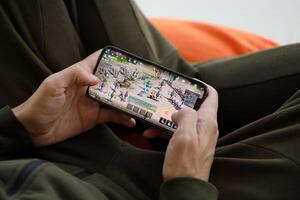 Lineage M mobile iOS game on iPhone 15 smartphone screen in male hands during mobile gameplay photo