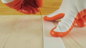 A worker draws a cutting line on a wood surface with a pencil. A worker in work gloves draws a line on a wood board. Low-angle view in close-up video