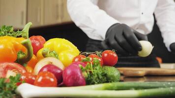 Professional chef cut a white onion in a thin slice on a wooden chopping block. Fresh vegetables in the foreground, low-angle view video
