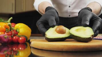 Fresh sliced avocado with bone on the kitchen table. Experienced chef in black rubber gloves cuts avocado and puts on a wooden chopping board video