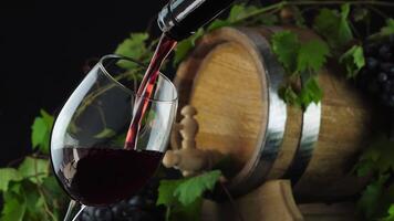 Wine. Red wine pouring from the bottle into a wineglass. Oak barrel for wine and ripe grapes with green leaves on background video