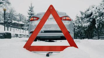 Car in the snow. Emergency warning triangle in foreground. Vehicle is stopped on the road with hazard lights on. video
