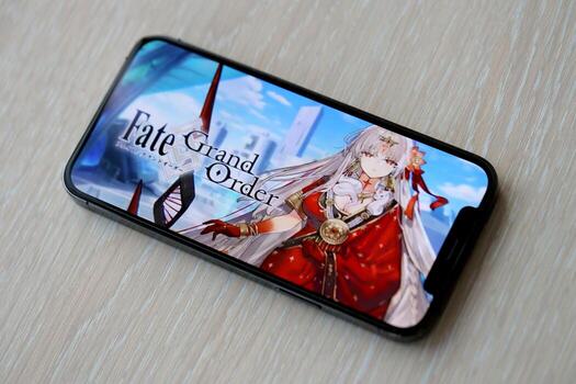 Fate Grand Order mobile iOS game on iPhone 15 smartphone screen on wooden table during mobile gameplay photo