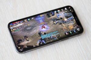 Lineage M mobile iOS game on iPhone 15 smartphone screen on wooden table during mobile gameplay photo