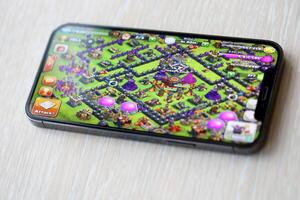Clash of Clans mobile iOS game on iPhone 15 smartphone screen on wooden table during mobile gameplay photo