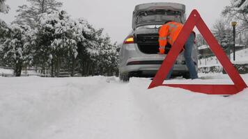 Car in the snow. Driver takes out gloves from the trunk. Emergency warning triangle in foreground. Vehicle is stopped on the road with hazard lights on. video