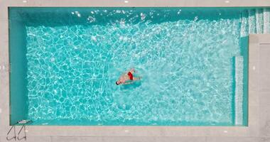 Top down view of a man in red shorts swims on his back in the pool. video