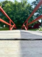 The empty wooden brown bridge top with blur background of green tree, red railing and blue sky. Exuberant image. photo
