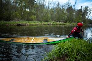 adventurous kayaker in a bright green kayak practicing the eskimo roll technique in a calm river surrounded by lush vegetation during an overcast day photo