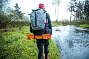 solo trekker with a large backpack and red beanie standing by a forest stream, ready for an adventure in the wilderness, embodying the spirit of exploration and nature photo